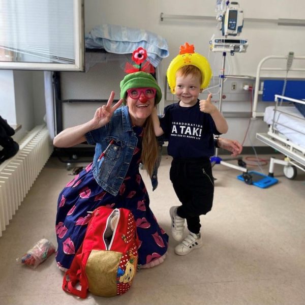 Liam og hospitalsklovnen Luna er på en hospitalsstue. De har hatte på og giver håndtegn