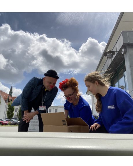 Emma og hospitalsklovnene Boing og Frøken Lakrids kigger ned i en papkasse med en fugl i