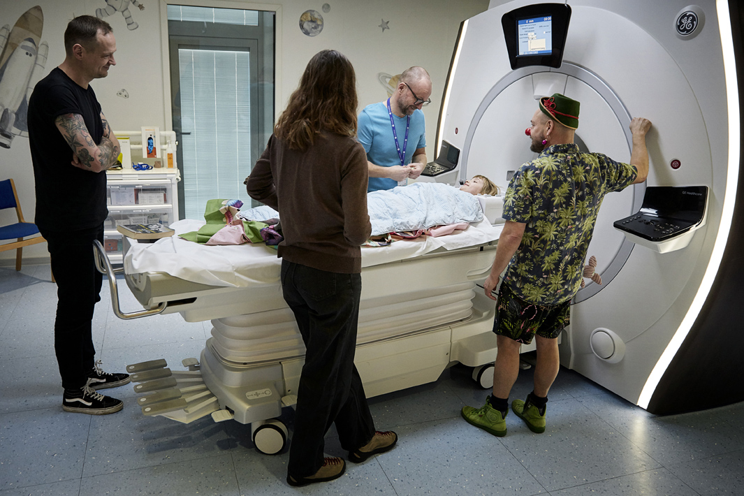 En radiograf, en hospitalsklovn og en kvinde står foran en MR-scanner, hvor der ligger en pige i