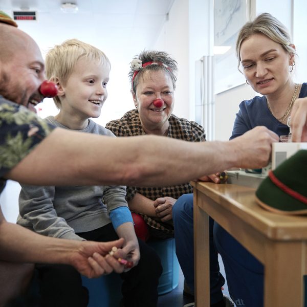 To hospitalsklovne, en radiograf og en dreng sidder omkring et bord, hvorpå der står en mini MR-scanner