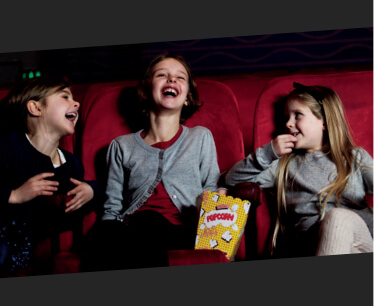 Tre børn i biografen. De griner og spiser popcorn.