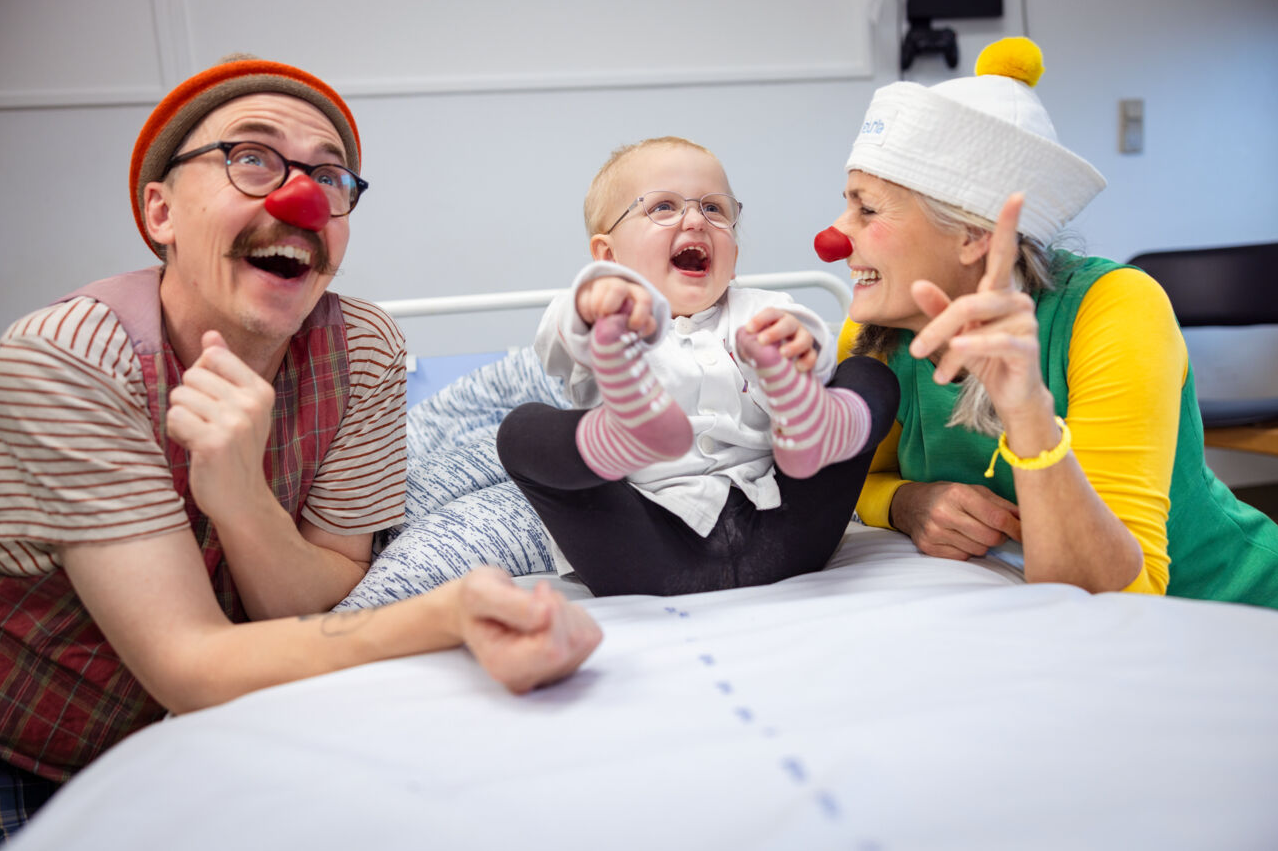 En lille pige ved navn Agnes i en hospitalsseng. Hun holder fast i sine fødder og griner stort. Ved siden af hende sidder de to hospitalsklovne, Petunia og Turbo.