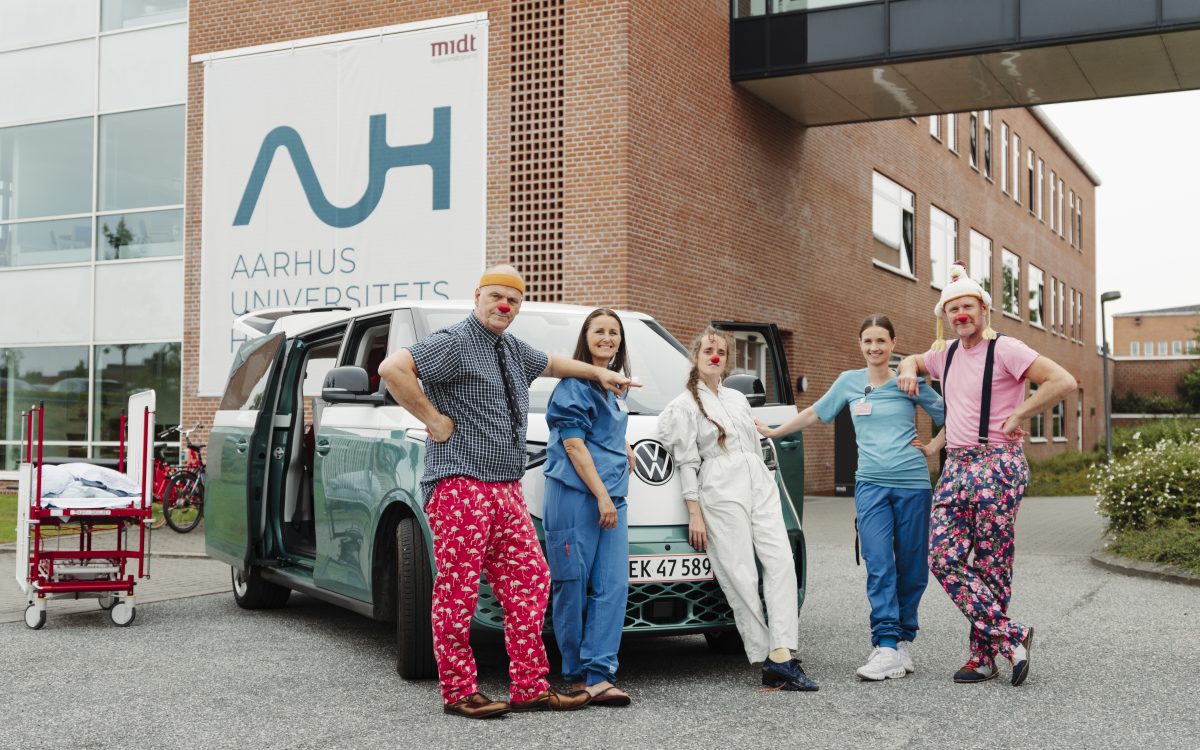 Tre hospitalsklovne og to sygeplejersker står foran AUH og Klovnbulancen.