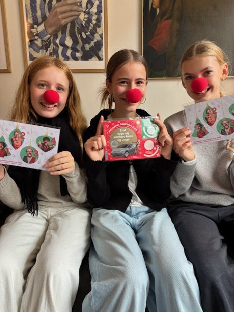 To unge piger, Alberthe og Ella, sælger Klovnenes Julelotteri. De har røde næser på.